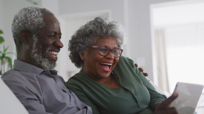 一对老非裔美国夫妇在家大笑。隔离期间的社交距离