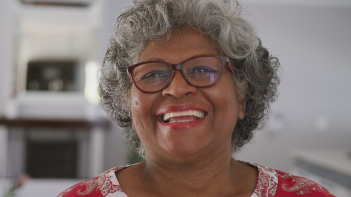 一位年长的非裔美国女性在社交距离中对着镜头微笑