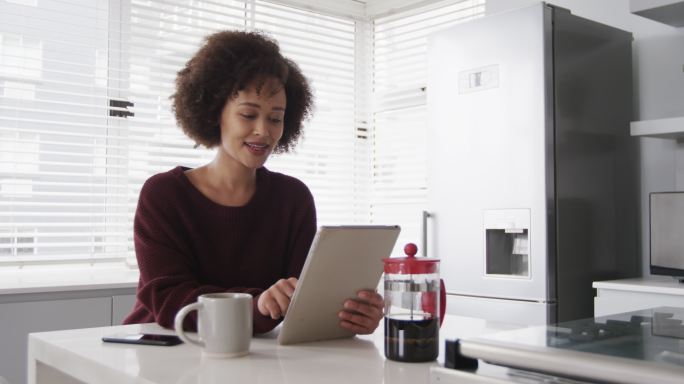 女人用着平板电脑，在厨房喝着咖啡