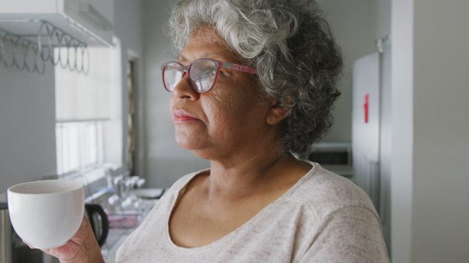 一个年长的非裔美国妇女在家里拿着一个杯子。隔离期间的社交距离