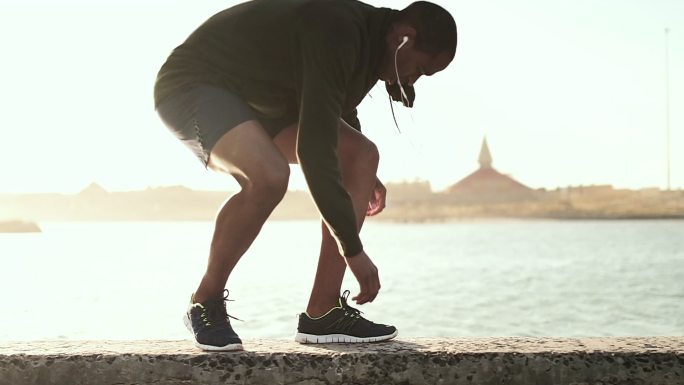 一名男子一边系鞋带一边在人行道上跑步