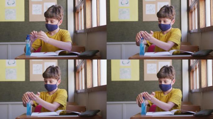 一个男孩坐在学校的课桌上，戴着口罩消毒双手