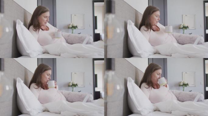 一个女人在家里的床上一边喝咖啡一边用笔记本电脑视频聊天