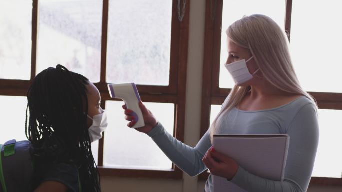 女老师戴着口罩在学校测量女生上课的温度