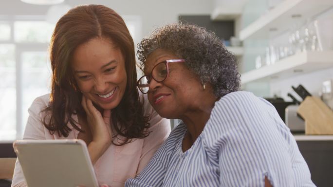 高级混血女性和她的女儿在社交距离中使用电子平板电脑