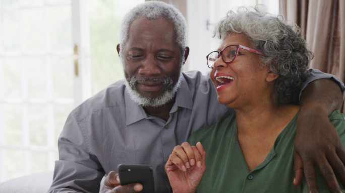 一对老非裔美国夫妇在家大笑。隔离期间的社交距离
