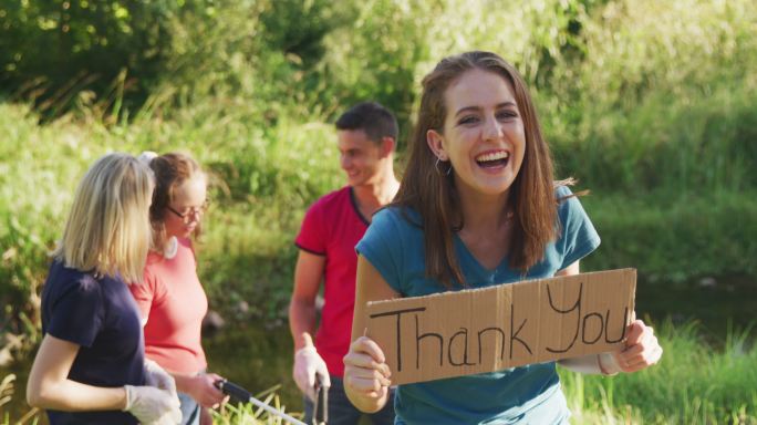 在河流清理日，中年人微笑着看着镜头和一个女人举着“谢谢你”的牌子