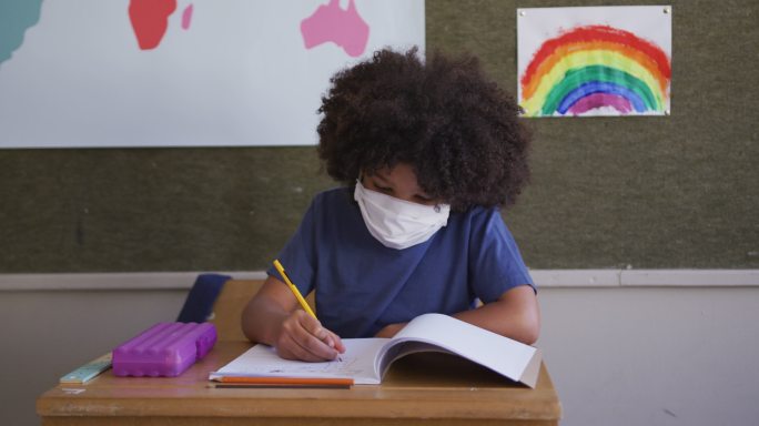 男孩戴着口罩在学校的桌子上写字