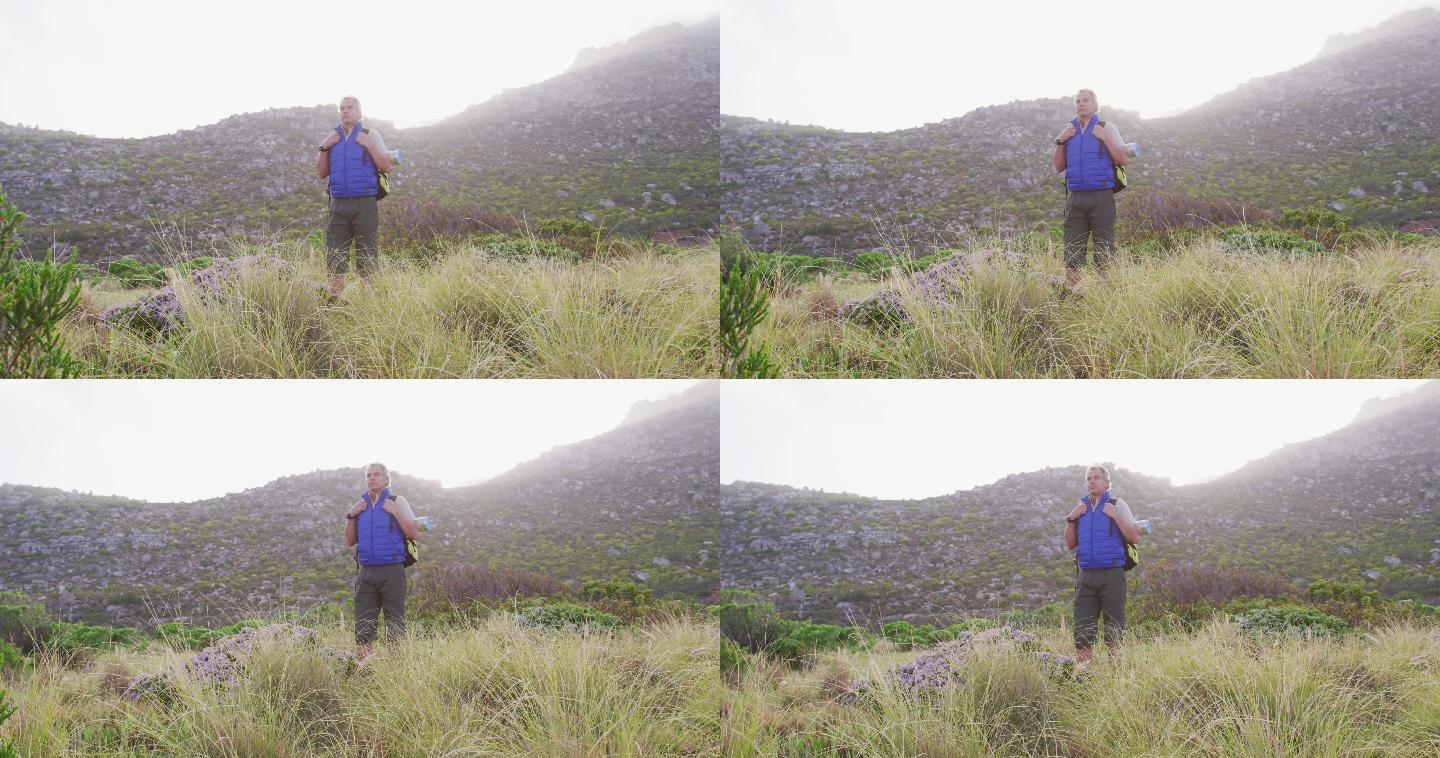 一个背着背包的老徒步者站在山上的草地上。徒步旅行