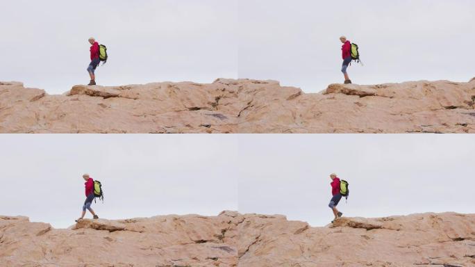 年长的徒步妇女背着背包，拄着拐杖在岩石上行走
