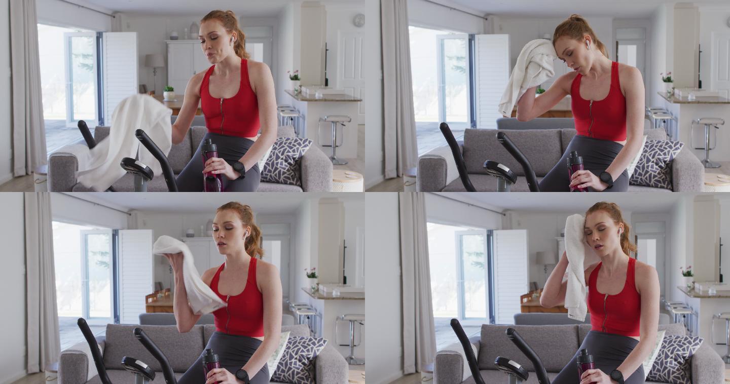 女人喝着水，坐在家里的健身自行车上用毛巾擦脸