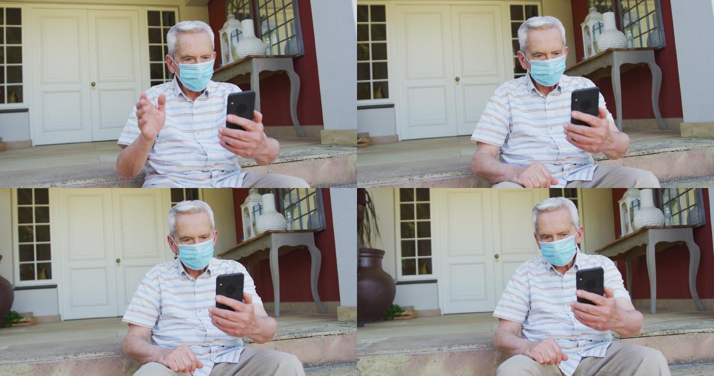 高级白人男子戴着口罩用智能手机视频聊天