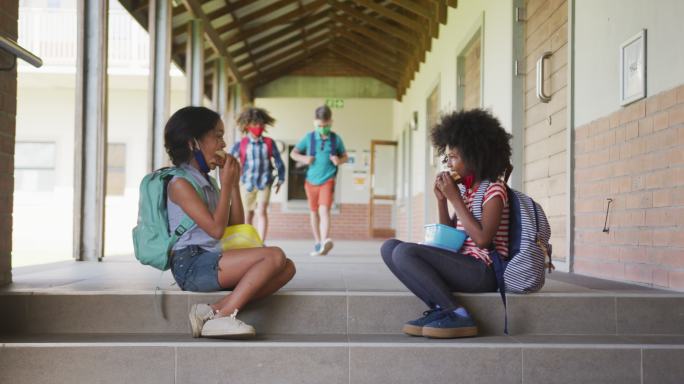 两个女孩坐在学校的楼梯上吃午餐盒饭