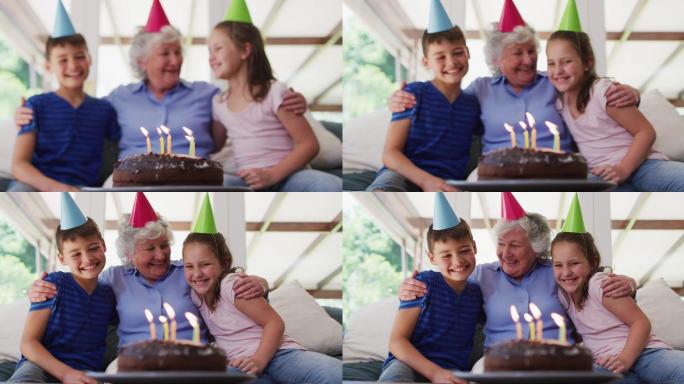 白人年长妇女在派对帽子拥抱她的孙子和生日蛋糕在桌上在家