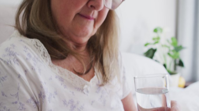 Senior woman holding pills and glass of water at h