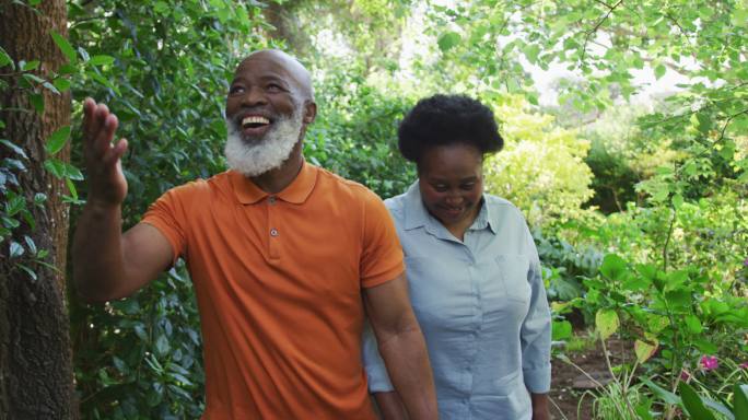 一对非洲裔美国老年夫妇手牵着手微笑着一起在花园里散步