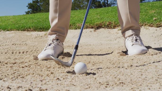低部分的白人老年人打高尔夫球出一个沙坑在一个明亮的高尔夫球场