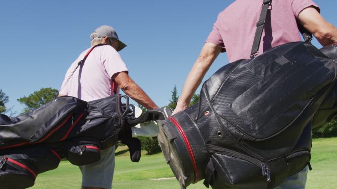 两名白种老人戴着口罩，拿着高尔夫球袋在高尔夫球场散步