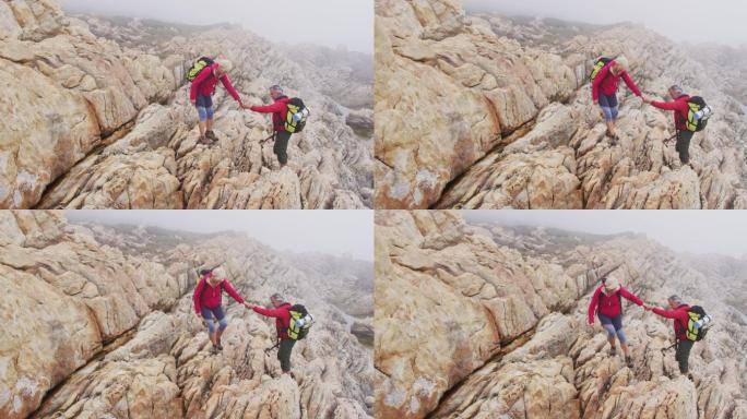 一对背着背包、拄着登山杖的资深徒步夫妇在攀岩时彼此牵着手