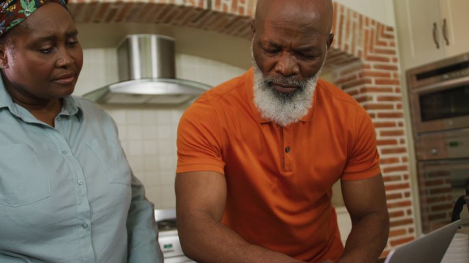 忧心忡忡的非洲裔美国老年夫妇账单使用笔记本电脑在家里的厨房