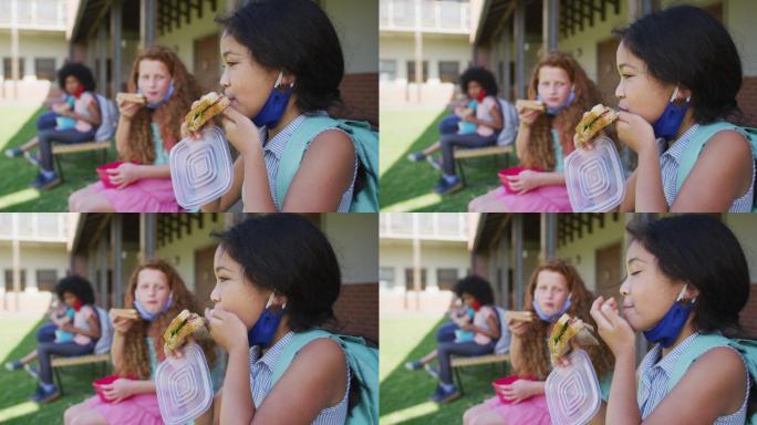 两个女孩坐在学校公园的长凳上吃午餐盒饭