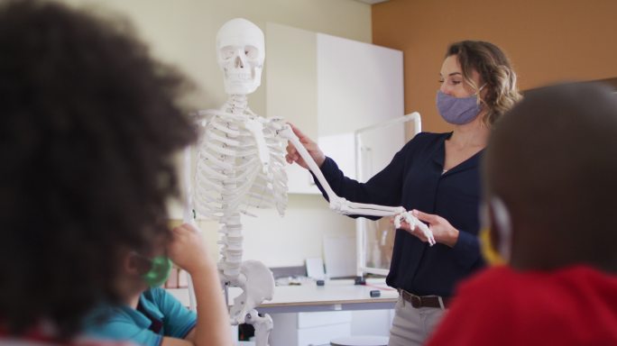 女老师戴着面具用人体骨骼模型给学生上课