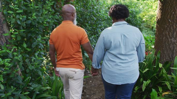 后视图的非洲裔美国老年夫妇牵手一起走在花园里