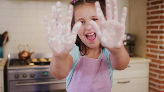 在家里的厨房里，一个白人女孩穿着围裙，手上沾着面粉