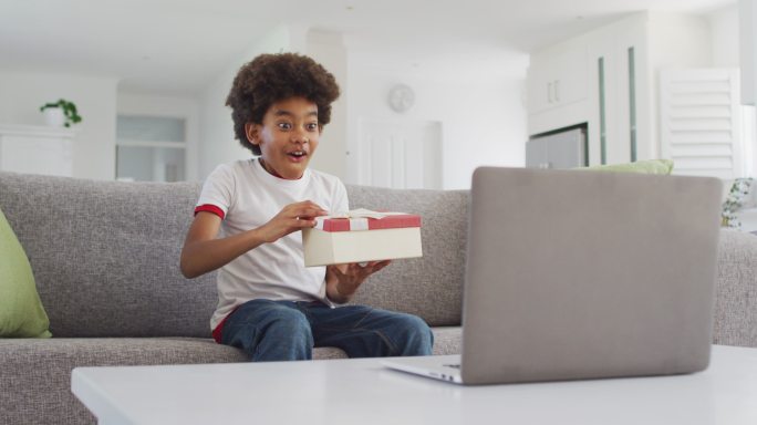 小男孩打开礼盒，同时在他的笔记本电脑上视频聊天