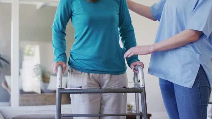 女性保健工作者在家中协助老年妇女用步行架走路