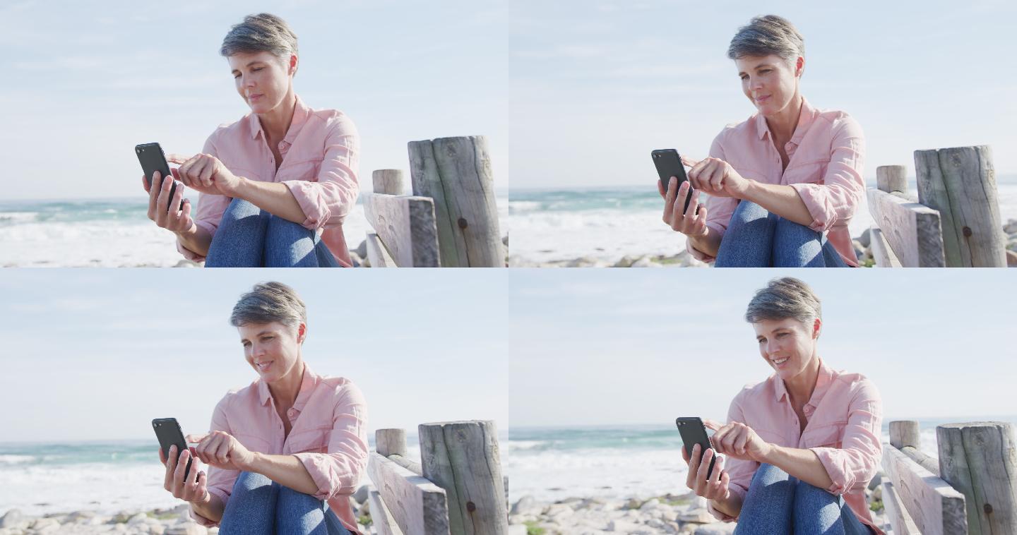 白人妇女享受自由时间在阳光明媚的一天使用智能手机海上