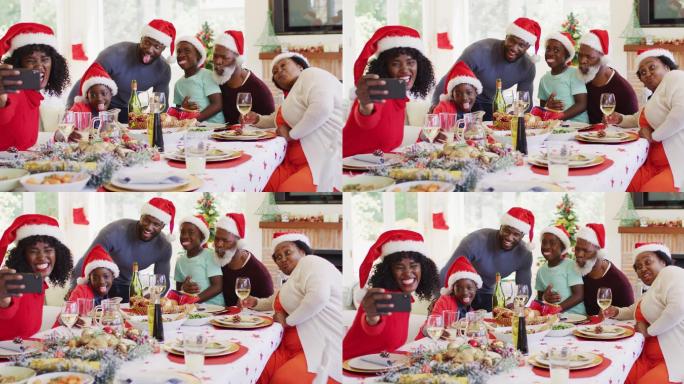 非裔美国家庭戴着圣诞老人帽坐在餐桌上用智能手机自拍哈哈