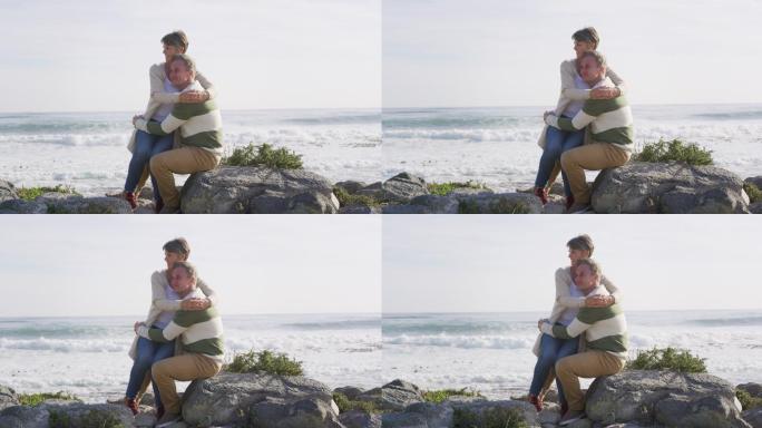 在阳光明媚的日子里，一对白种夫妇坐在海边拥抱，享受自由时光
