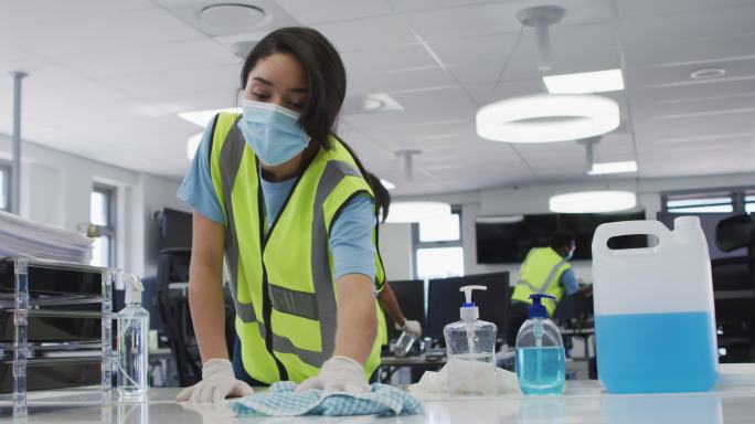 妇女穿着背心和面罩，用消毒剂清洁办公室
