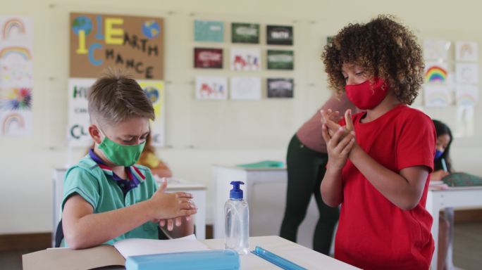 两个男孩戴着口罩在学校课堂上消毒双手