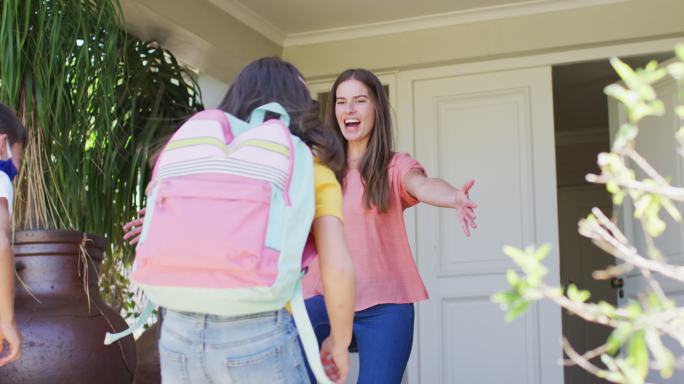 白人男孩和女孩戴着口罩拥抱他们的母亲放学后