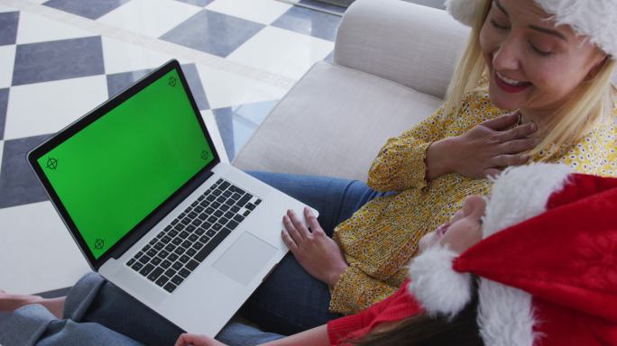 妈妈和女儿戴着圣诞帽在家里用笔记本电脑视频聊天