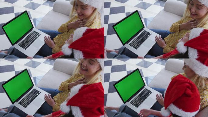 妈妈和女儿戴着圣诞帽在家里用笔记本电脑视频聊天