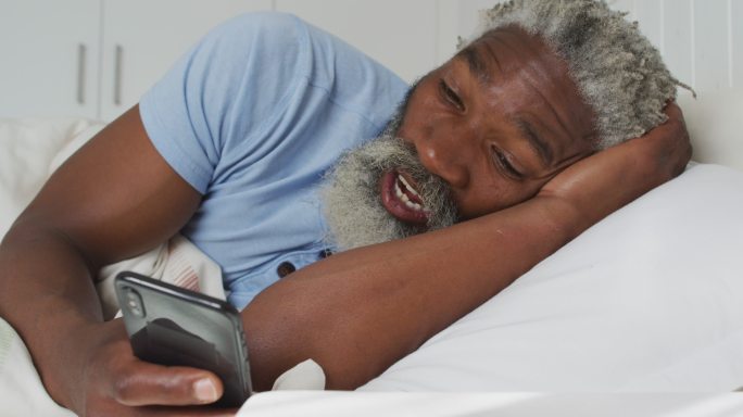 一位老人正在家里的床上用智能手机视频聊天