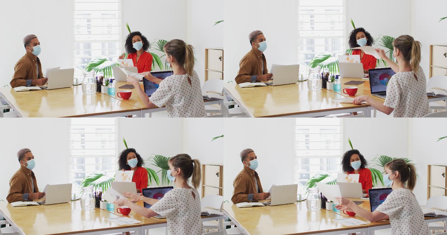 一名戴口罩的妇女在办公室向同事展示一份文件