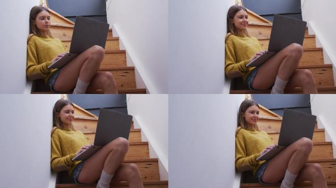 坐在家里楼梯上使用笔记本电脑的女人