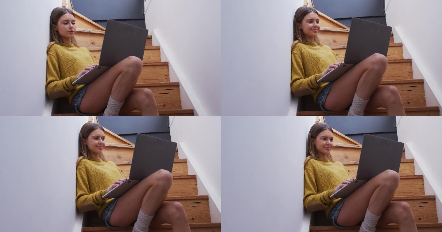 坐在家里楼梯上使用笔记本电脑的女人