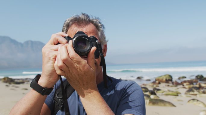 一名高级徒步旅行者在海滩上用数码相机拍照。