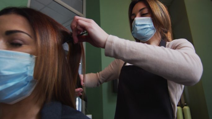 女发型师戴着口罩在发廊为女顾客拉直头发