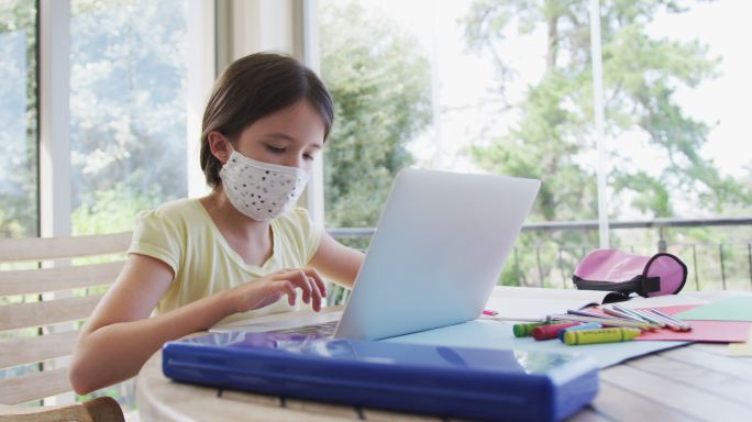 女孩戴着口罩在家里用笔记本电脑