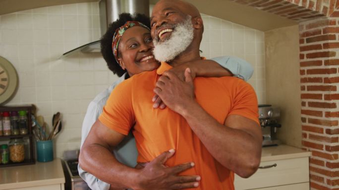 一对非裔美国老年夫妇在自家厨房里拥抱