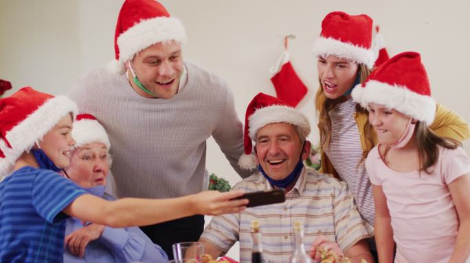 白人家庭戴着圣诞老人帽，脖子上戴着面具，一起使用智能手机