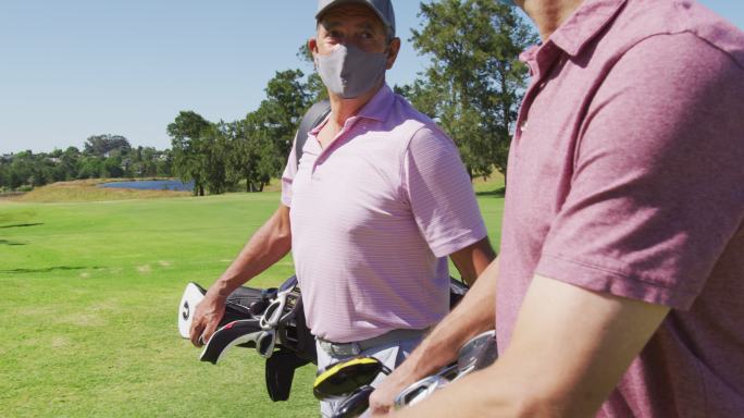 两名白种老人戴着口罩，拿着高尔夫球袋在高尔夫球场散步
