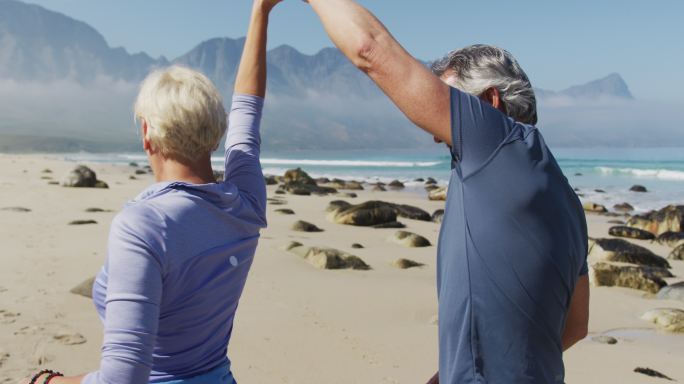 老年徒步旅行者夫妇一边徒步一边在海滩上跳舞。