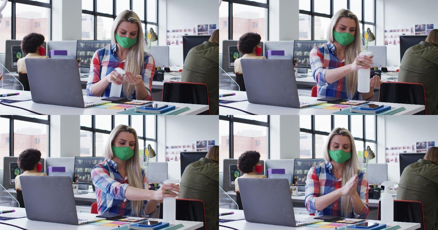 白人女商人戴着口罩在现代办公室用笔记本电脑消毒手